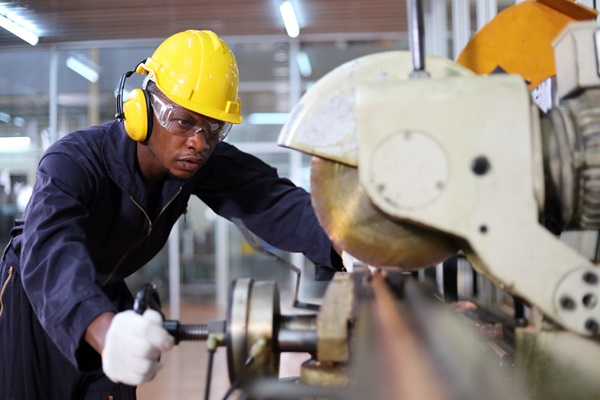 Factory worker wearing safety gear operates industrial machinery, highlighting workplace safety measures and potential risks in manufacturing environments.