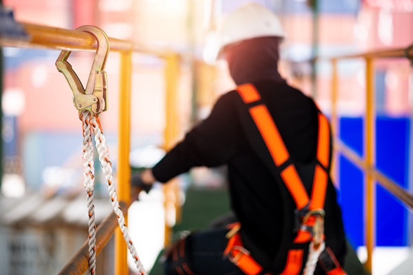 Construction worker wearing a safety harness and a safety line, working on a scaffold at height.