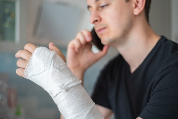 A man talking on a smartphone with his hand and wrist wrapped in a thick white gauze bandage after a work injury in Ohio.